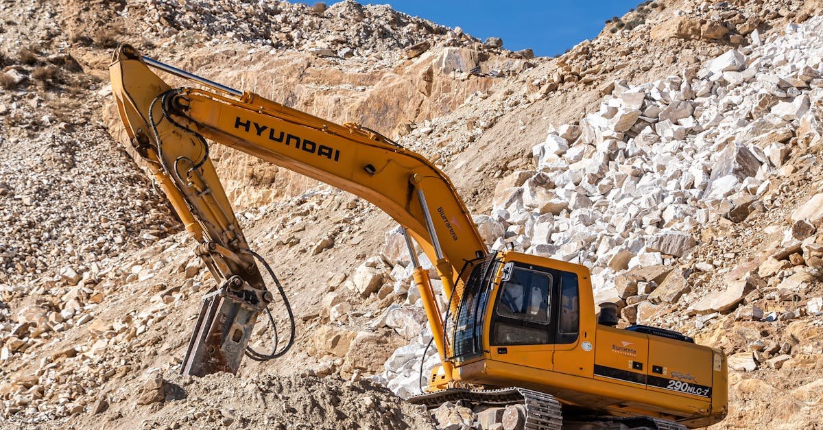 Yellow Hyundai excavator operating in a rocky quarry under a clear blue sky. Perfect for industrial themes.