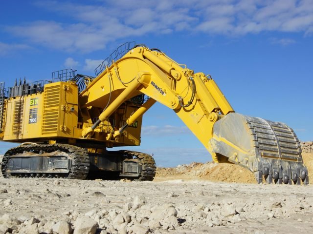 Yellow excavator in a sunny, open construction site, under a blue sky.