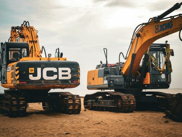 Two heavy excavators on a sandy beach, showcasing industrial construction machinery.